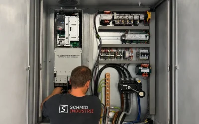 Servicetechniker von Schmid Industrie repariert einen Frequenzumrichter im geöffneten Schaltschrank eines Industriekompressors.