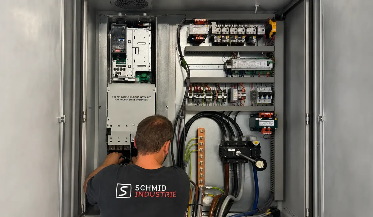 Servicetechniker von Schmid Industrie repariert einen Frequenzumrichter im geöffneten Schaltschrank eines Industriekompressors.